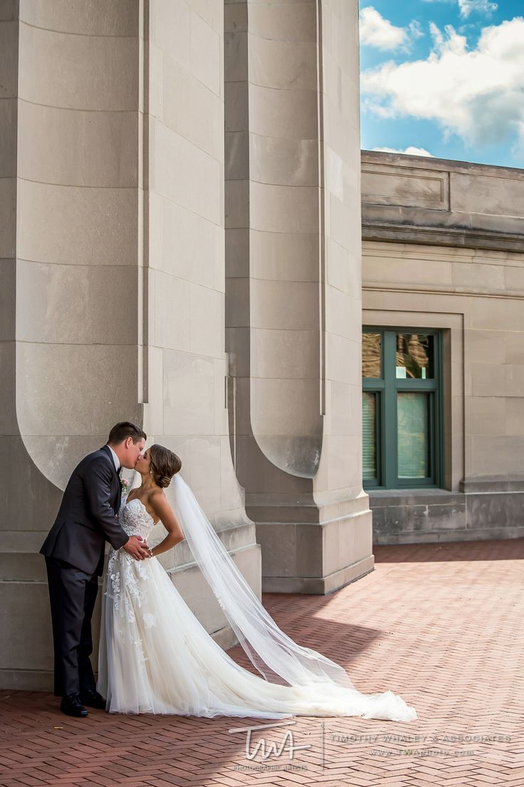 a bride and groom kissing in front of an old building with columns on either side