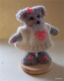 a small gray teddy bear wearing a white sweater and pink flowers on it's head