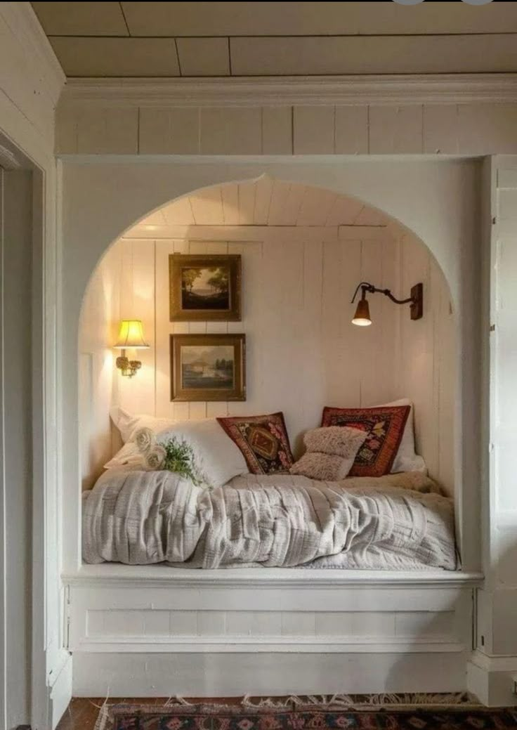 a white bed sitting under a window next to a rug on top of a wooden floor