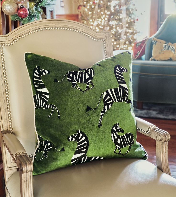 a green pillow with zebras on it sitting on a chair in front of a christmas tree