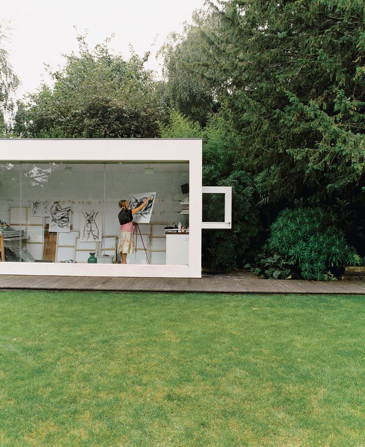 a woman is painting on the outside of a white building with trees in the background