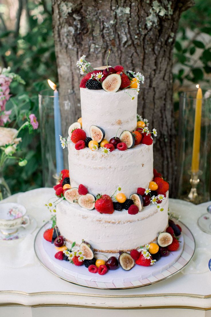 a three tiered cake with fresh fruit on the top is displayed in front of a tree