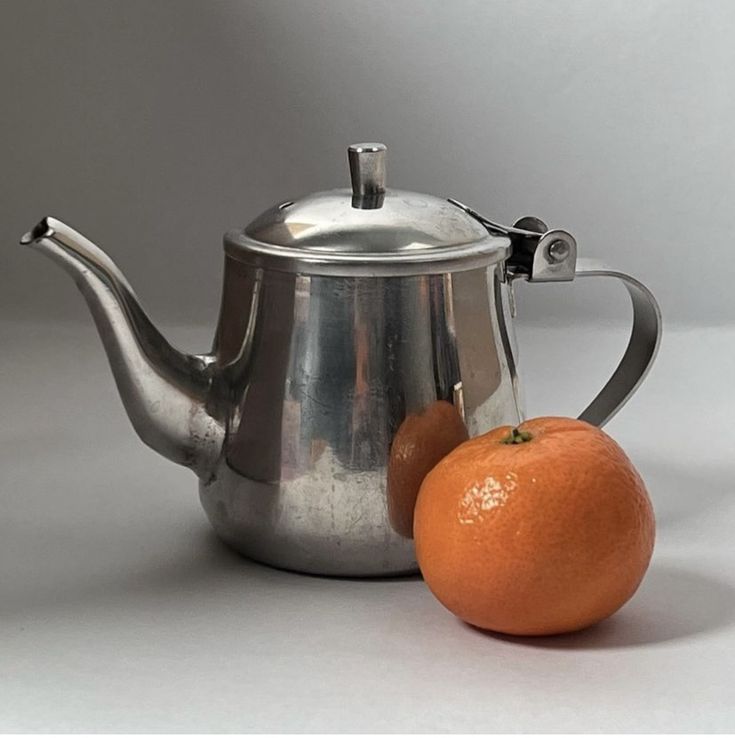 an orange sitting next to a silver tea pot