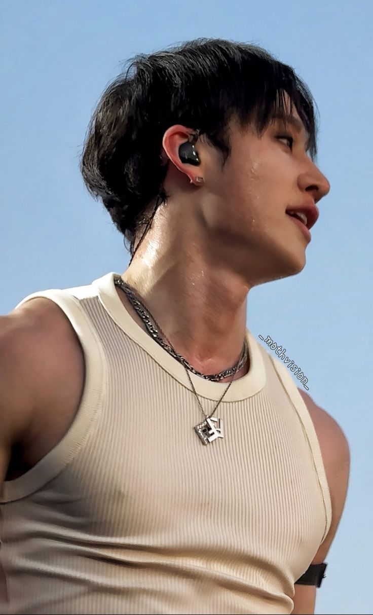 a young man with ear buds on his ears wearing a tank top and silver necklace