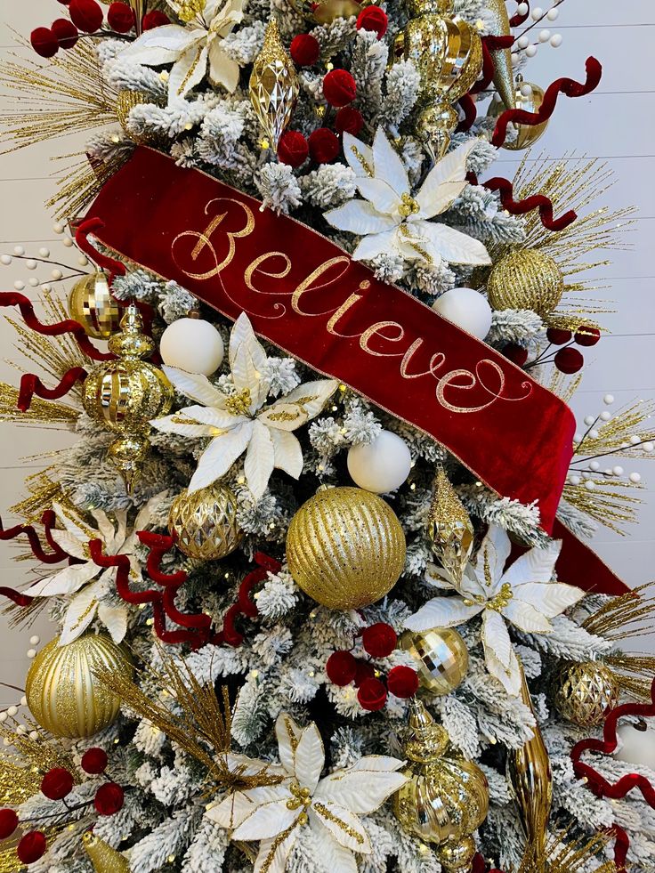 a christmas tree decorated with red and gold ornaments, white poinsettis and bells