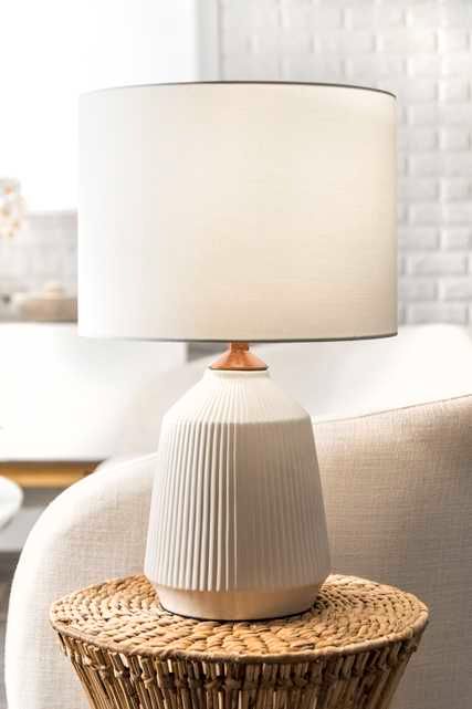 a white lamp sitting on top of a wicker table next to a beige chair