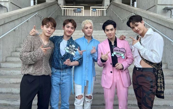 four young men posing for a photo in front of some stairs with their thumbs up