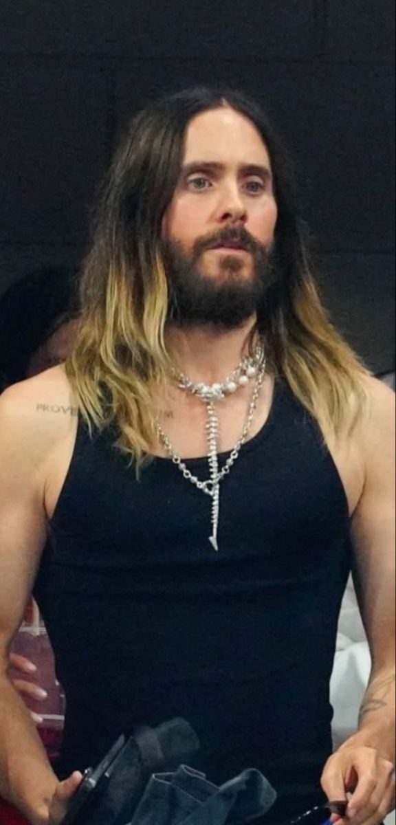 a man with long hair wearing a black tank top and silver chain around his neck