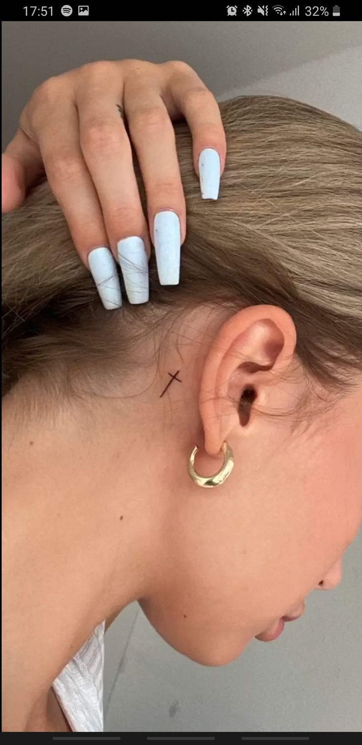 a woman's ear with white acrylic nails and a cross tattoo on it