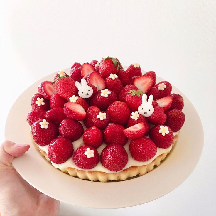 a cake with strawberries and rabbits on top is being held by a person's hand