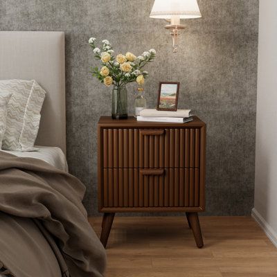 a nightstand with flowers on it next to a night stand and lamp in a bedroom