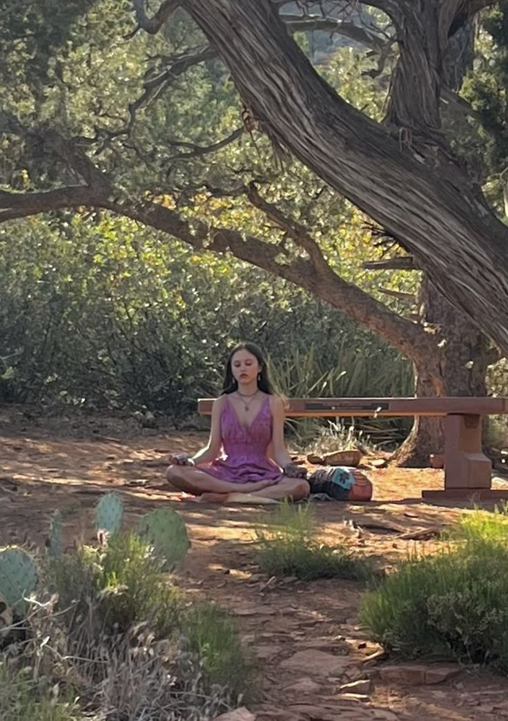 a woman sitting in the middle of a forest doing yoga