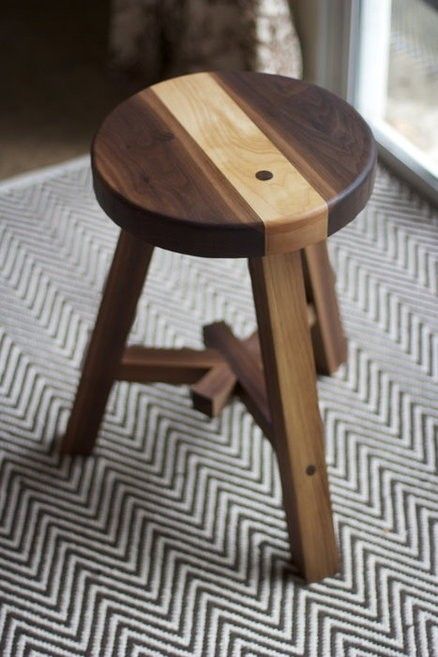 a small wooden stool sitting on top of a carpeted floor next to a window