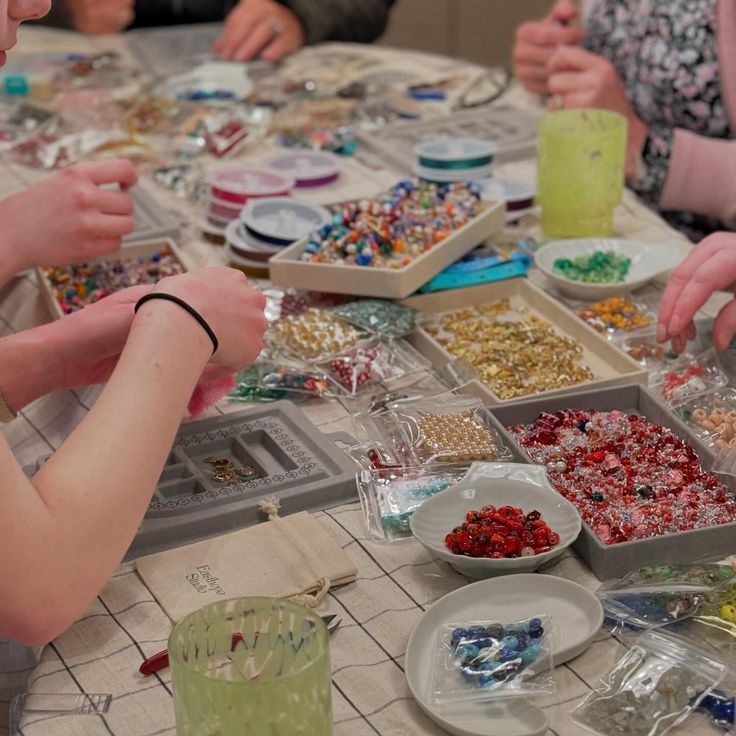 several people are sitting at a table making beads