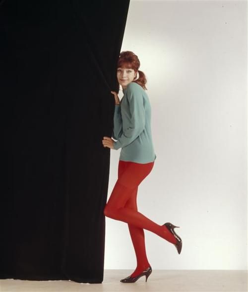 a woman in red tights leaning against a black curtain