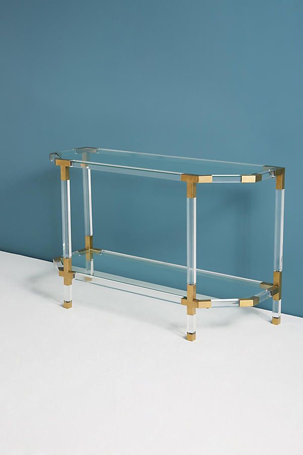 a glass and brass console table against a blue wall