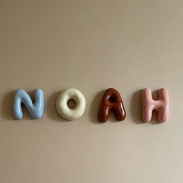 the word noah spelled out in ceramic letters on a beige wall with two donuts