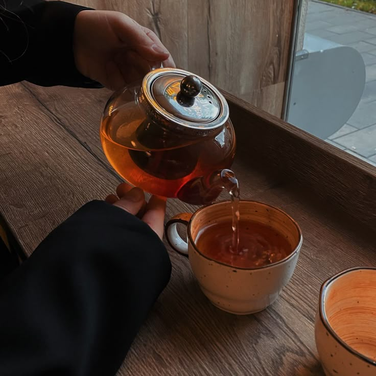 a person pouring tea into a cup on a wooden table