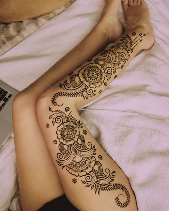 a woman laying on top of a bed with her legs covered in hendi tattoos