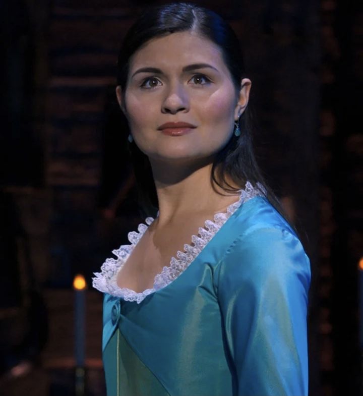 a woman in a blue dress standing next to candles and looking off into the distance