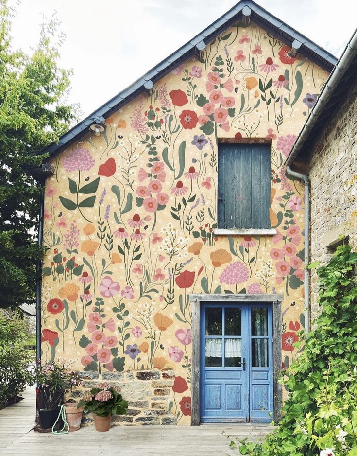 an old building with flowers painted on the side and blue door, in front of it