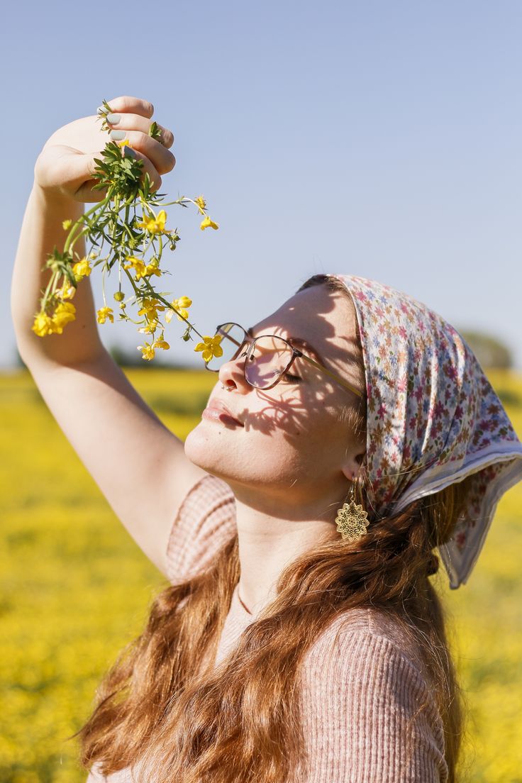 a woman with glasses and a flower in her hair is standing in the middle of a field