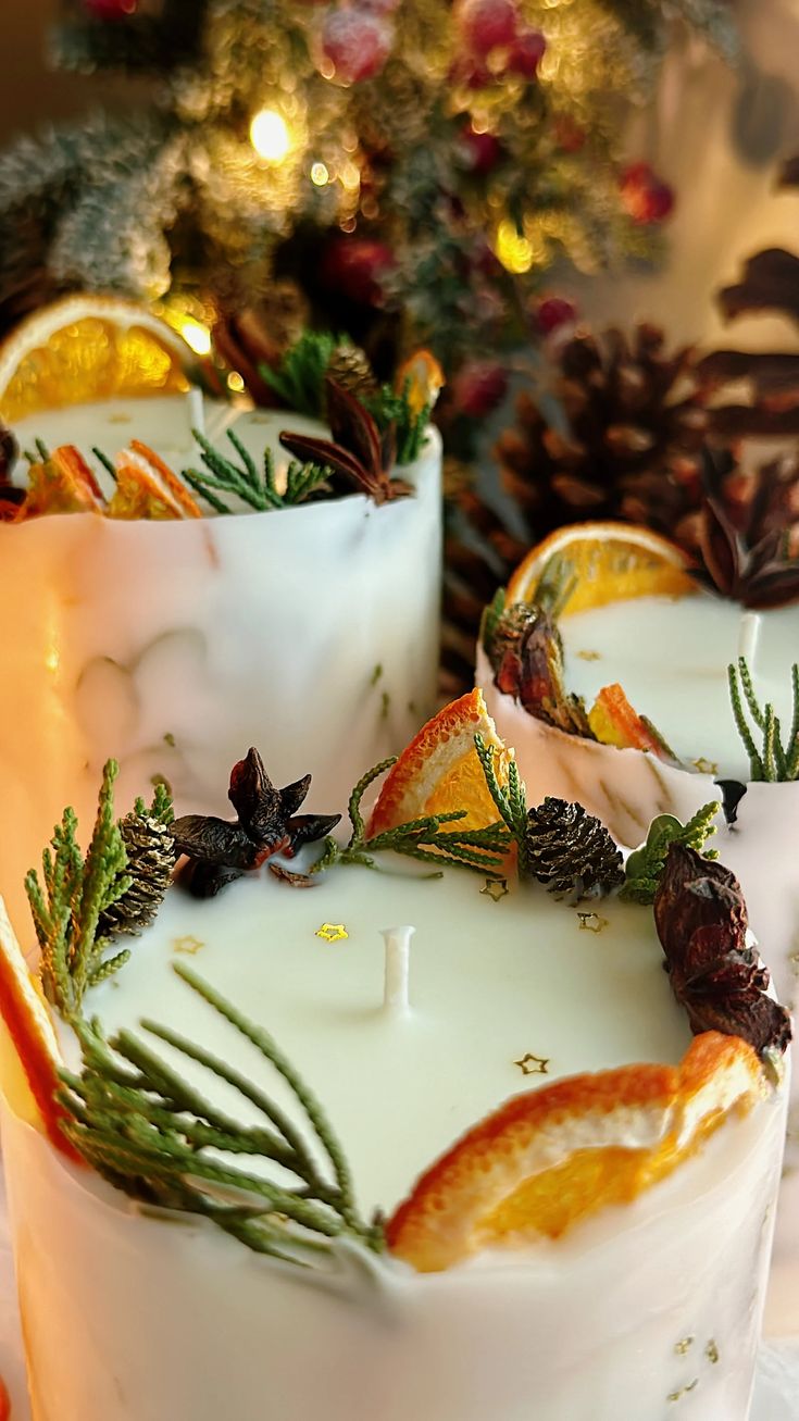 two white candles sitting on top of a table next to pine cones and oranges