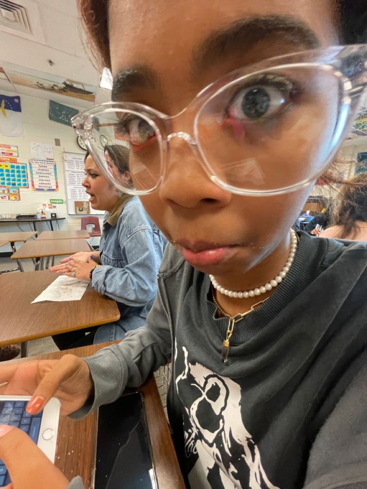 a girl wearing glasses looking at the camera while using a laptop computer in a classroom