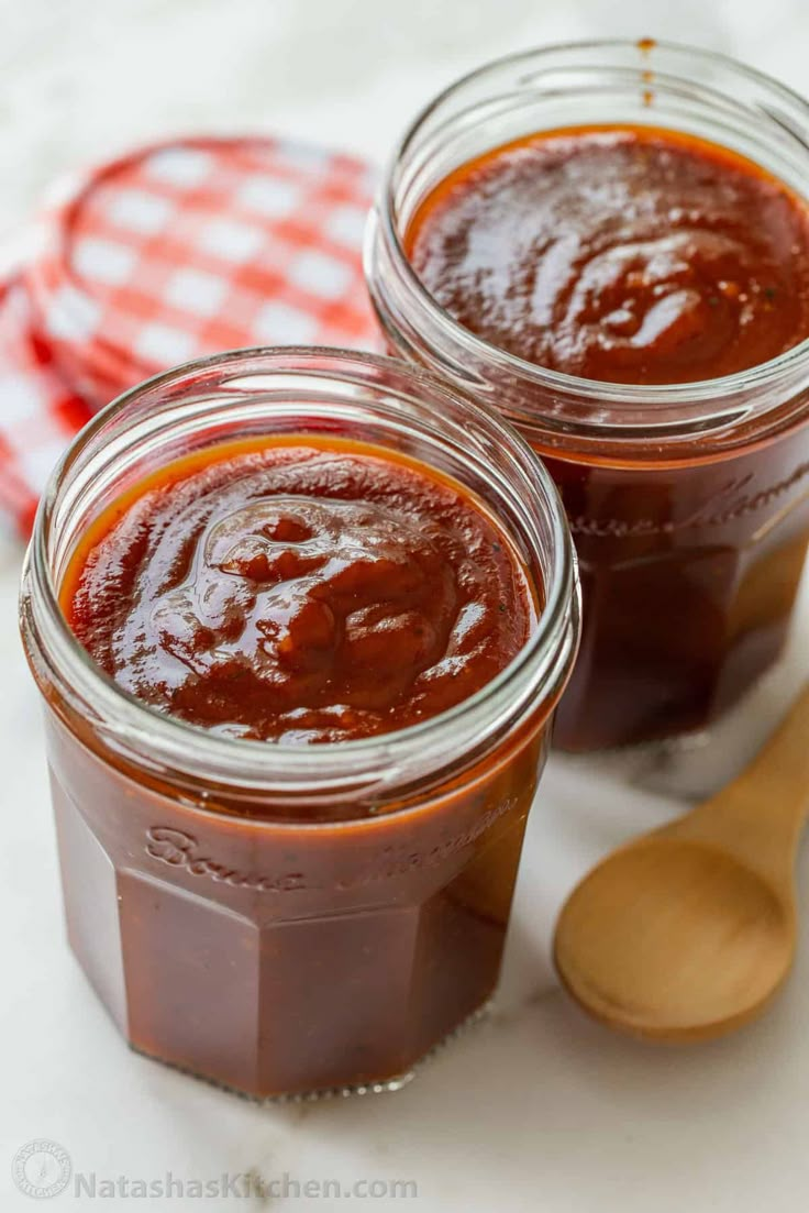 two jars filled with chocolate pudding sitting on top of a table next to a wooden spoon