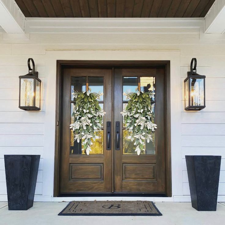 the front door is decorated with wreaths and two large planters on either side