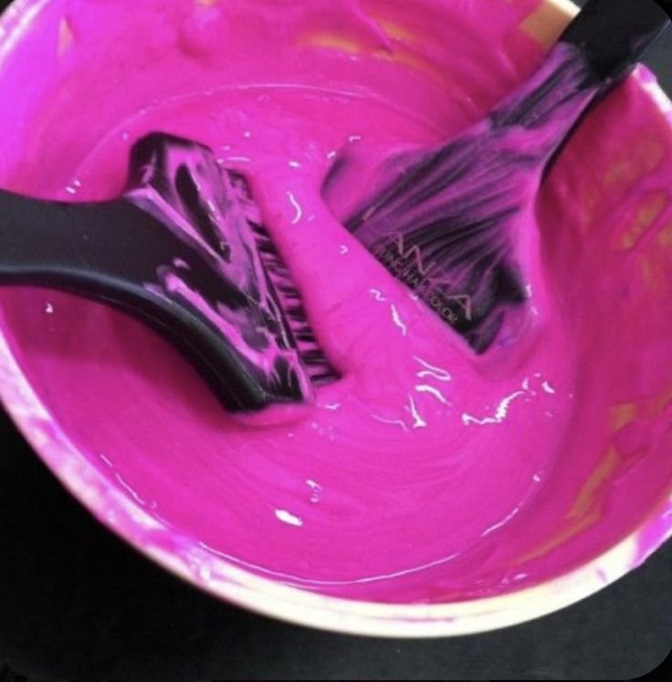 two black brushes in a pink bowl with purple paint on the inside and one brush sticking out of it