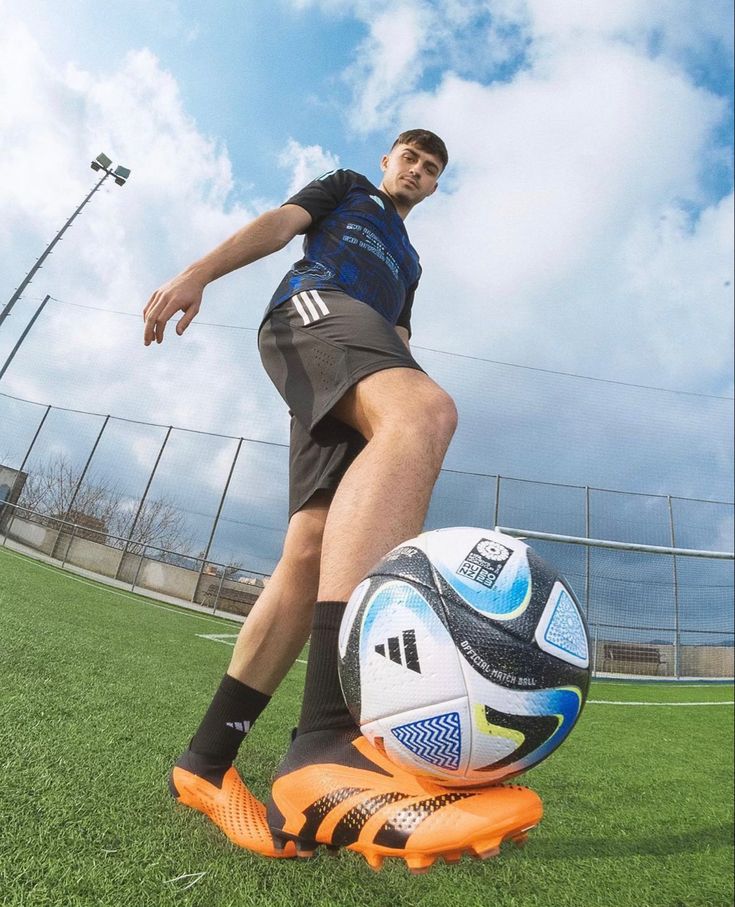 a man standing next to a soccer ball on top of a green field with blue sky in the background