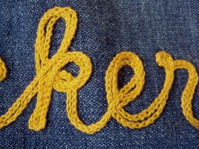 the word crochet written in yellow yarn on a pair of blue jean pants