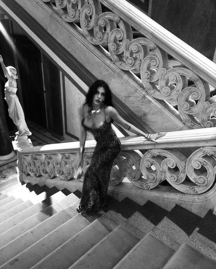 black and white photograph of a woman sitting on the handrail of a stair case