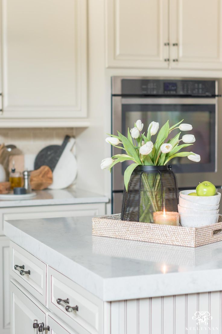 a vase with flowers and an apple on a kitchen counter