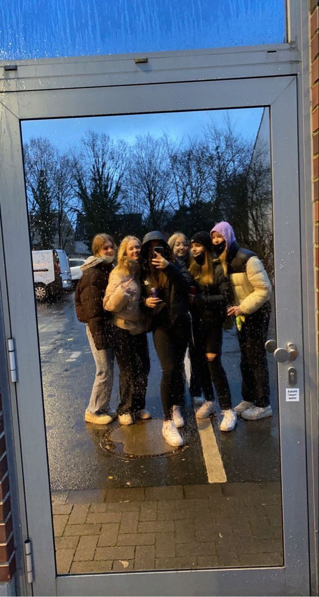 a group of people standing in front of a glass door on a sidewalk with the reflection of trees behind them