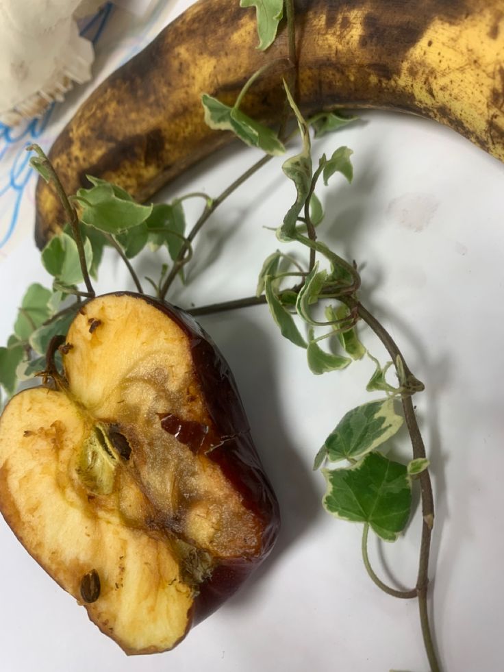 an apple is cut in half and sitting next to a banana on a white surface