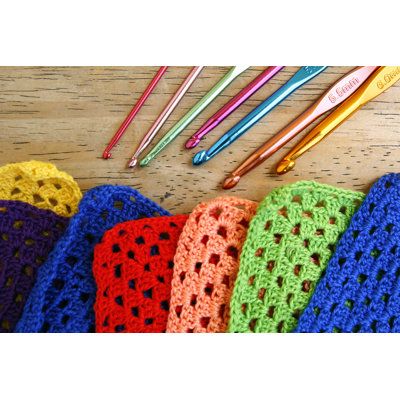 crocheted cloths are lined up on a table with knitting needles in the background