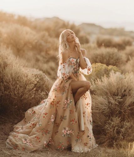 a woman in a long dress sitting on the ground with her legs crossed and looking off to the side