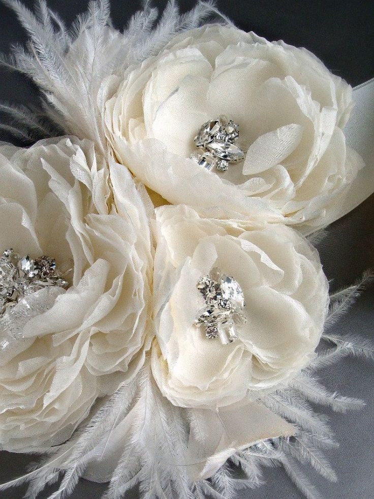 three white flowers with crystal centers on a silver cloth headband and some feathers in the background