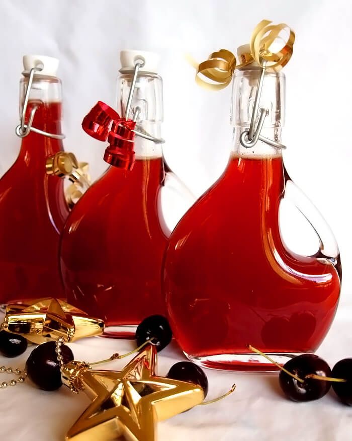 three red bottles with gold accents and cherries on a white tablecloth, one is filled with wine