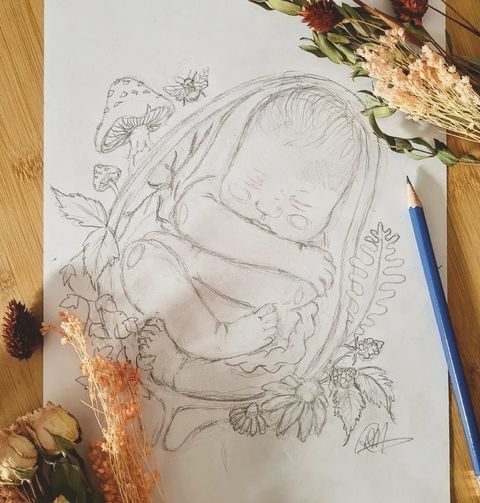 a drawing of a baby in a basket surrounded by dried flowers and leaves on a wooden table