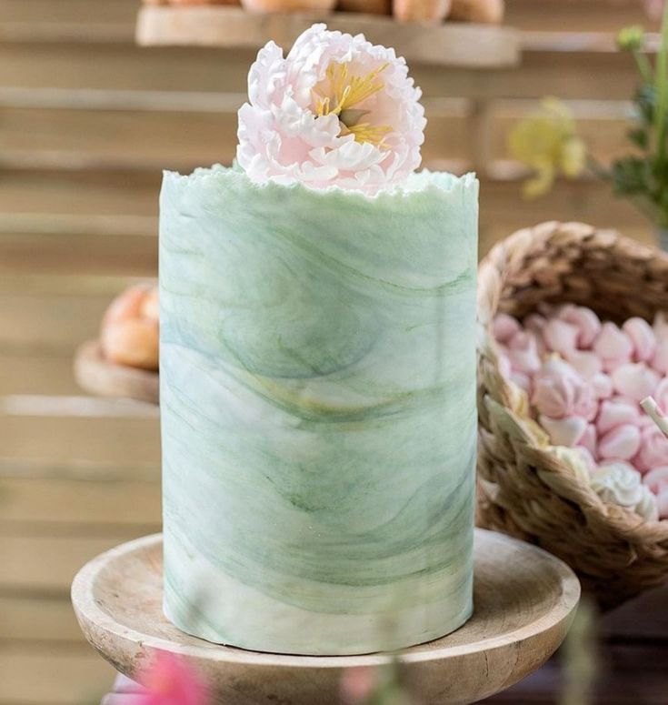 a green marbled cake with pink flowers on top and other pastries in the background