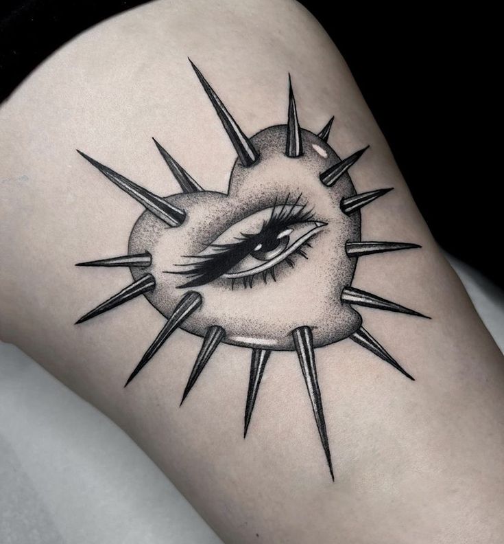 a woman's thigh with an eye and spikes tattoo on the side of her leg