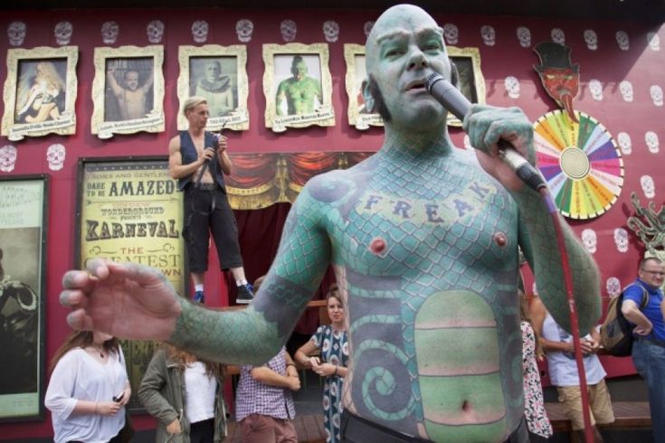 a man with green paint on his body holding a microphone in front of a group of people