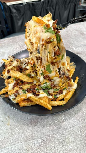 a black plate topped with cheesy french fries and cheese covered in toppings