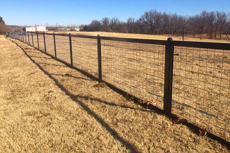 a black fence in the middle of a field with brown grass and trees behind it