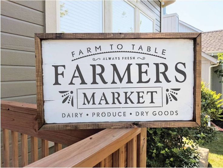 a sign that says farmers market on the side of a wooden porch next to a house