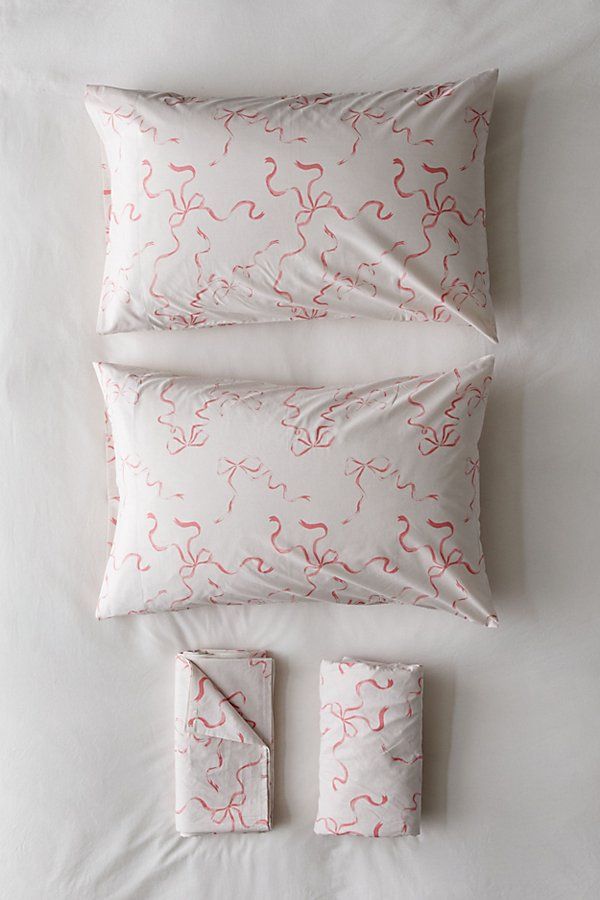 a white bed with pink and red designs on the pillow cases, pillows and sheets