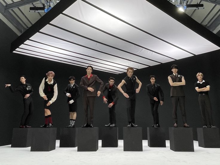 a group of young men standing on top of black blocks in front of a white ceiling